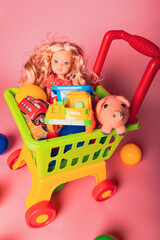 Colorful toy shopping cart with dolls, cars, and animals sitting on a pink background
