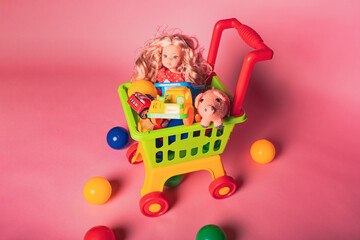 Colorful toy shopping cart with dolls, cars, and animals sitting on a pink background