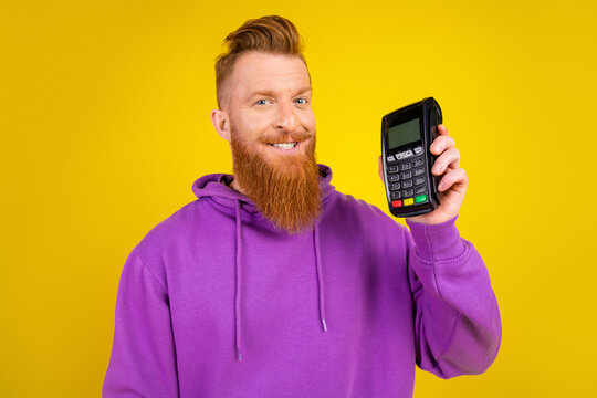 Young bearded man in purple hoodie smiling while presenting a card reader against a yellow background