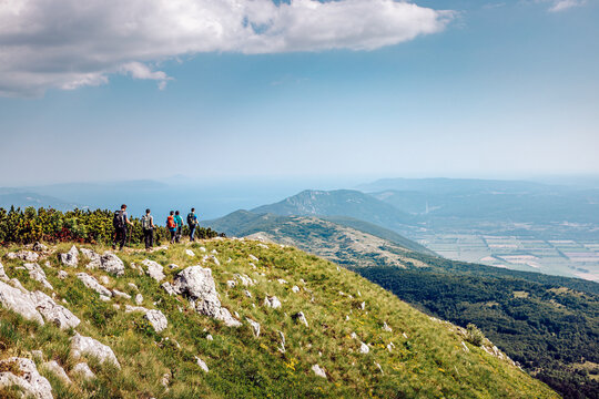 View of hikers silhouetted against the expansive sky, standing atop the grassy peak, gazing over the Adriatic Sea, Mala Ucka, Primorje-Gorski Kotar County, Croatia.