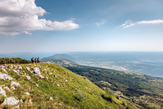 View of hikers silhouetted against the horizon atop a grassy peak, overlooking a vast valley under a bright sky, Mala Ucka, Primorje-Gorski Kotar County, Croatia.