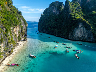 Aerial view of boats floating on turquoise waters, framed by towering limestone cliffs cloaked in emerald foliage, Tambon Ao Nang, Chang Wat Krabi, Thailand.