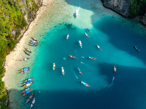 Aerial view of turquoise waters embrace traditional boats near a lush coastline, creating a vibrant tapestry of blues and greens, Tambon Ao Nang, Chang Wat Krabi, Thailand.