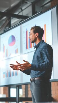 Young male executive explains financial statistics and analytics to colleagues using digital graphs in a contemporary workspace. Visual storytelling enhances corporate communication and growth
