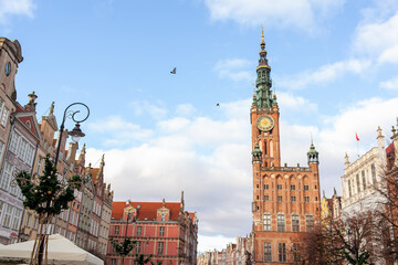 Obraz premium A clock tower stands tall in city sqare. Street in an Old town and Town Hall in Gdansk, Poland. Panoramic view. Historical city of Gdansk (Danzig), Poland, Europe.
