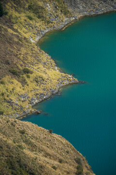 View of the striking turquoise lake water contrasting sharply with the rugged, grassy slopes of the volcanic crater rim, Quilotoa lake, Cotopaxi province, Ecuador.