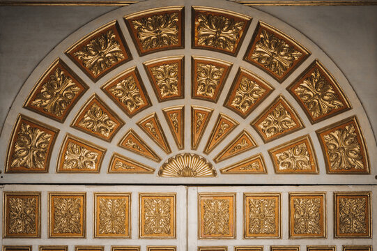 View of gilded floral carvings radiating in a semi-circular pattern above ornate panels, a rich display of craftsmanship, Quito, Ecuador.