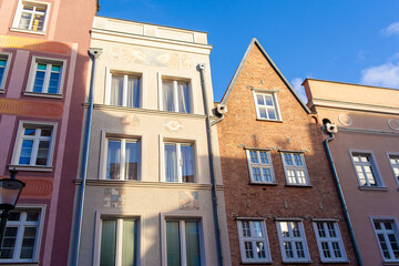 Distinct buildings share a street, showcasing diverse architectural styles and colors under bright sunlight in Gdansk, Poland