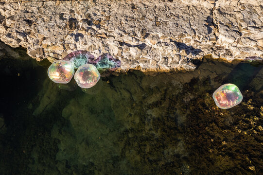 Aerial view of iridescent bubbles floating on the clear water next to the rocky coast, Ahtopol Lighthouse, Ahtopol, Bulgaria.