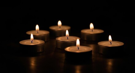 Seven tealight candles, flames aglow, in dim surrounding