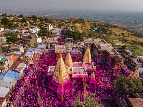 Aerial view of a vibrant temple complex awash in pink hues, contrasting with the surrounding buildings and verdant landscape, Jyotiba Dongar, Maharashtra, India.