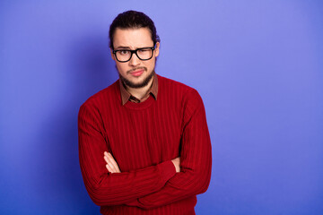 Young handsome man with glasses in a red sweater stands with arms crossed against a purple...