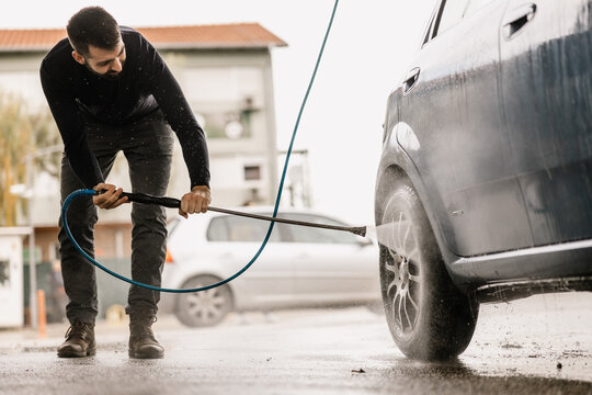 Man using high pressure washer to clean car at self service station