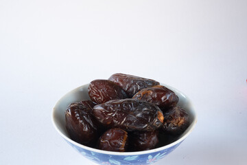Bowl filled with dark brown dates on white background
