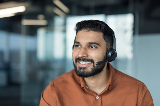 Indian man smiling while wearing a headset, working in a modern office environment, confidently providing excellent customer service and professional technical support