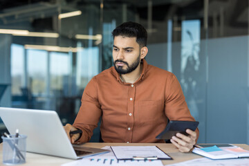 Young businessman or accountant checking financial data, using a calculator and laptop while...