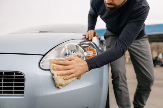 Close-up of a man cleaning car headlight with cloth during auto detailing service, focusing on vehicle maintenance and cleanliness.