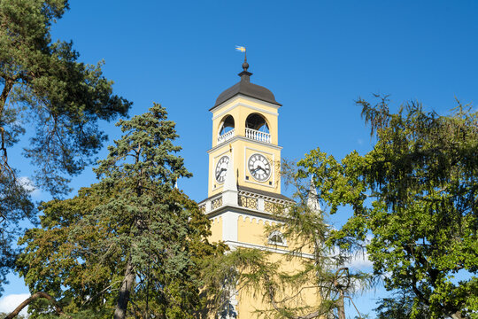 View of Amiralitetsklockstapeln clock tower standing tall from below, framed by vibrant green foliage under blue sky, Karlskrona, Blekinge County, Sweden.