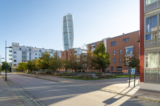 View of the Turning Torso skyscraper rises majestically behind low-rise brick buildings and leafy trees under a clear blue sky, Vastra Hamnen, Malmo, Sweden.