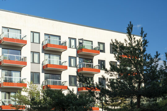 View of modern architecture with white walls and vibrant orange balconies contrasting against the deep blue sky and green trees, Vastra Hamnen, Malmo, Sweden.