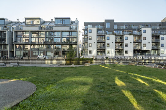 View of modern architecture reflecting in the canal's still waters, a lush green lawn bathed in sunlight, and a serene atmosphere, Vastra Hamnen, Malmo, Sweden.