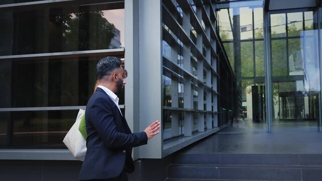 An Indian man and a caucasian woman walk side by side while chatting, then the shot opens as they enter a modern office lobby with more people inside. Urban business mood, teamwork and arrival.