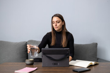 Woman drinking water working home using tablet