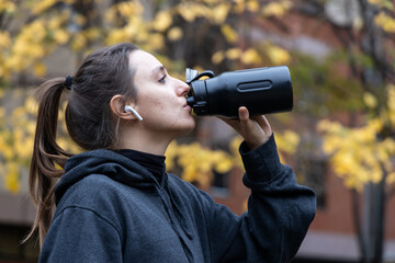 Woman hydrating with water bottle during autumn outdoors