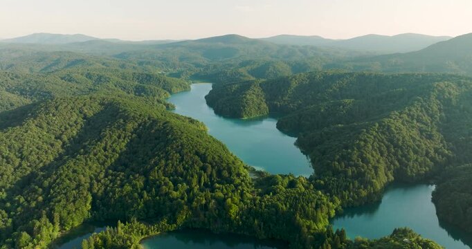 Aerial view of vibrant turquoise waters of Plitvice Lakes interwoven with dense green forests under a soft haze, Plitvice, Croatia.