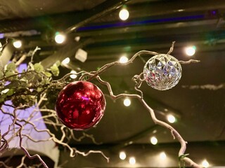 Red and silver Christmas ornaments hanging from branches, surrounded by soft glowing lights, creating a festive atmosphere for holiday celebrations and decorations