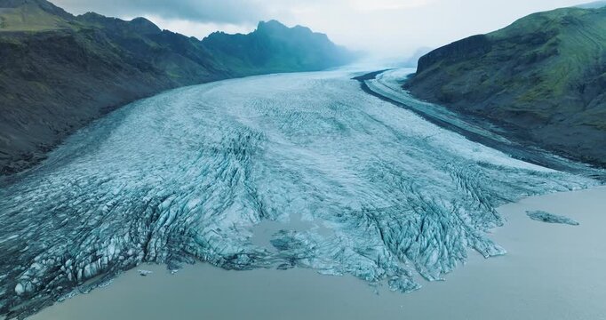 Aerial view of the majestic Skaftafellsjokull glacier flowing between rugged mountains into a glacial lake, Skaftafell, Iceland.