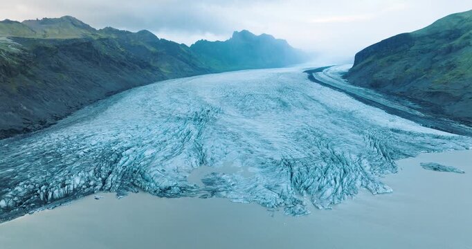 Aerial view of the glacial ice meeting the water, with contrasting tones and textures, framed by mountains, Skaftafell glacier, Iceland.