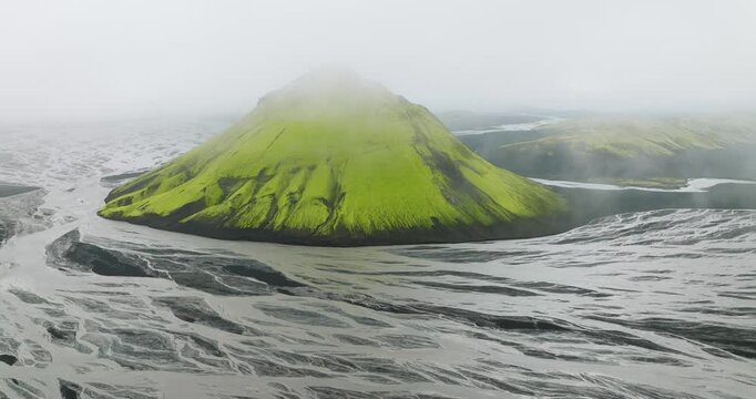 Aerial view of Maelifell mountain with its bright green slopes contrasting the grey braided rivers under a blanket of fog, Maelifell, Iceland.