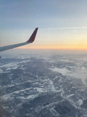 Airplane wing over winter landscape at sunrise from aerial view.