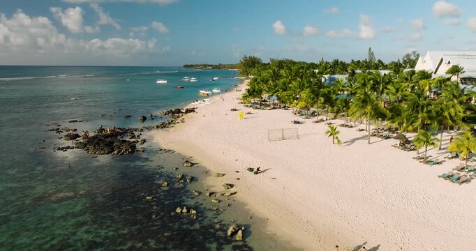 Aerial view of sun-kissed white sands meet the cerulean sea, fringed with swaying palms and distant boats, Grand Baie, Mauritius.