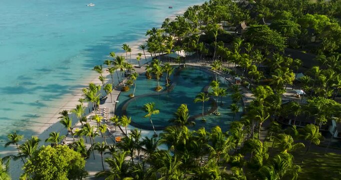 Aerial view of turquoise waters meet a verdant shoreline dotted with palm trees and a luxurious pool resort, Trou aux Biches, Mauritius.
