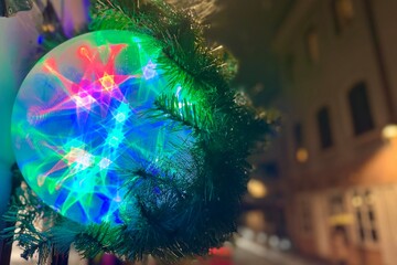 Colorful glowing spherical ball decoration against a city street with lights and bokeh. Festive atmosphere in the night urban environment. Christmas greeting card with copy space