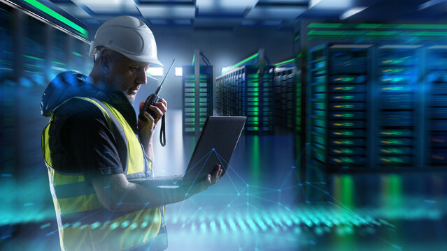 Data center technician monitors server systems using a laptop and radio. IT infrastructure support, network maintenance, cybersecurity operations, cloud service management. - Powered by Adobe