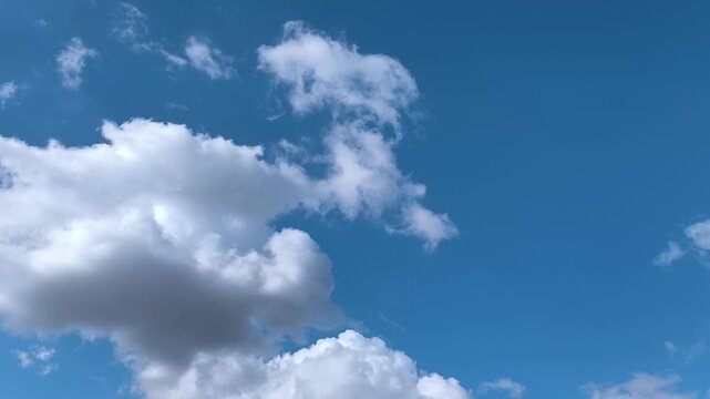 Dark cumulus clouds with some brightness moving across the blue sky