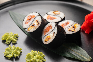 Yin yang sushi rolls with eel and salmon served on a black plate with wasabi and ginger