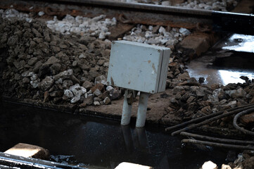 Railway track junction control box metal industrial wet water puddle rock gravel travel along old railway track reveals industrial control box near junction among metal and gravel, reflections