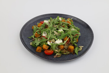 Grilled pumpkin salad with arugula and pumpkin seeds with oil on dark plate on a white background