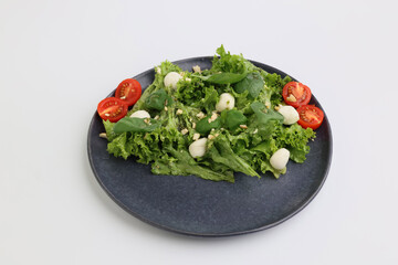 Summer fresh diet salad with cherry tomatoes, mozzarella cheese, basil and olive oil on dark plate on white background. Healthy lunch