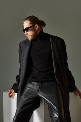 Obraz premium Elegant man in stylish coat and chic sunglasses poses in modern grey studio
