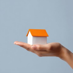 Naklejka premium Hand holding miniature house model with orange roof on grey background