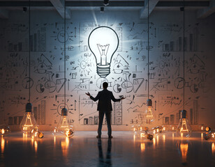 Businessman stands in front of light bulb artwork and data charts in office space during evening hours