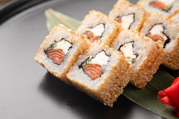 Sesame coated sushi rolls with fresh salmon and cream cheese served on a black plate with ginger