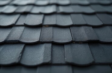 Close-up view of a dark grey asphalt shingle roof with a textured surface. Overlapping shingles create a repeating pattern. This image shows building exterior detail.