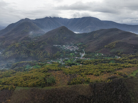 Aerial view of a patchwork of autumn colors blankets the rolling hills and valleys, nestled beneath a sky heavy with clouds, Serino, Irpinia, Italy.
