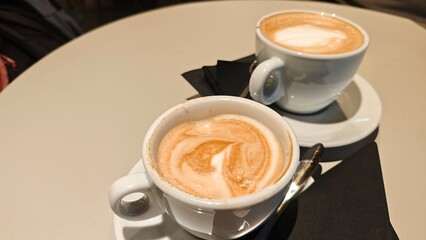 Two cups of cappuccino with creamy milk foam served on a round cafe table with spoons and napkins. Concept of shared coffee moment, social interaction and relaxed cafe lifestyle